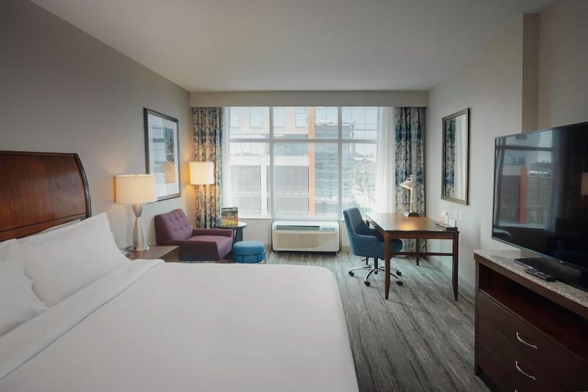A hotel room with a bed, a desk, a chair, a television, and a window with curtains.
