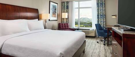 A hotel room with a large bed, a desk with a television, a chair, and a view of the outdoors.