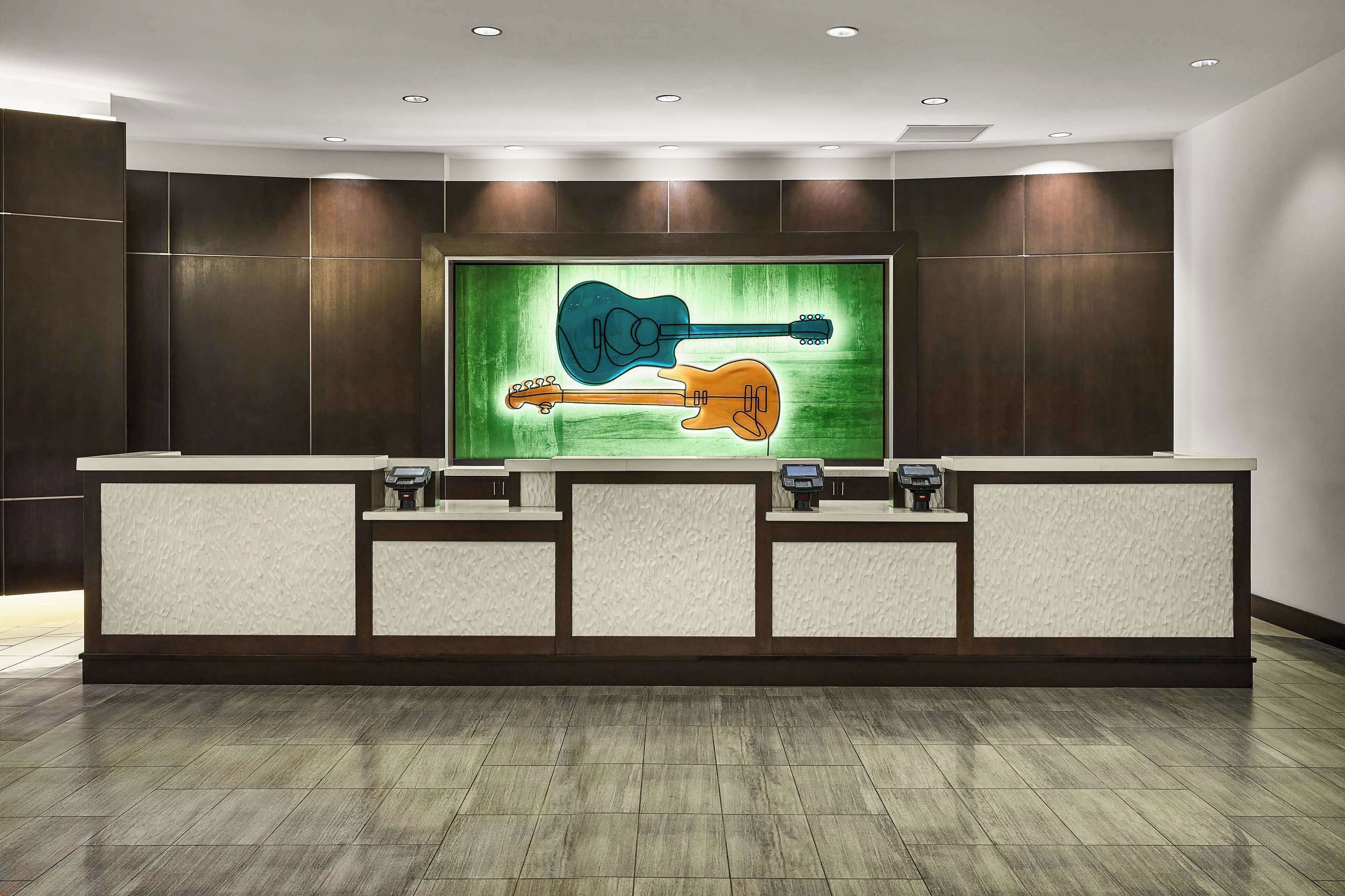 A reception desk with a large wall-mounted artwork of guitars, a modern design with recessed lighting and a dark wood finish.