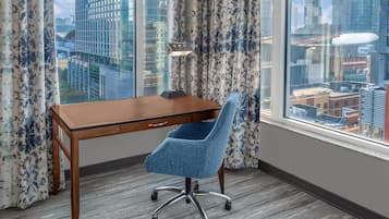 Ein moderner Arbeitsraum mit Schreibtisch aus Holz, einem blauen Bürostuhl und Stadtblick durch große Fenster.