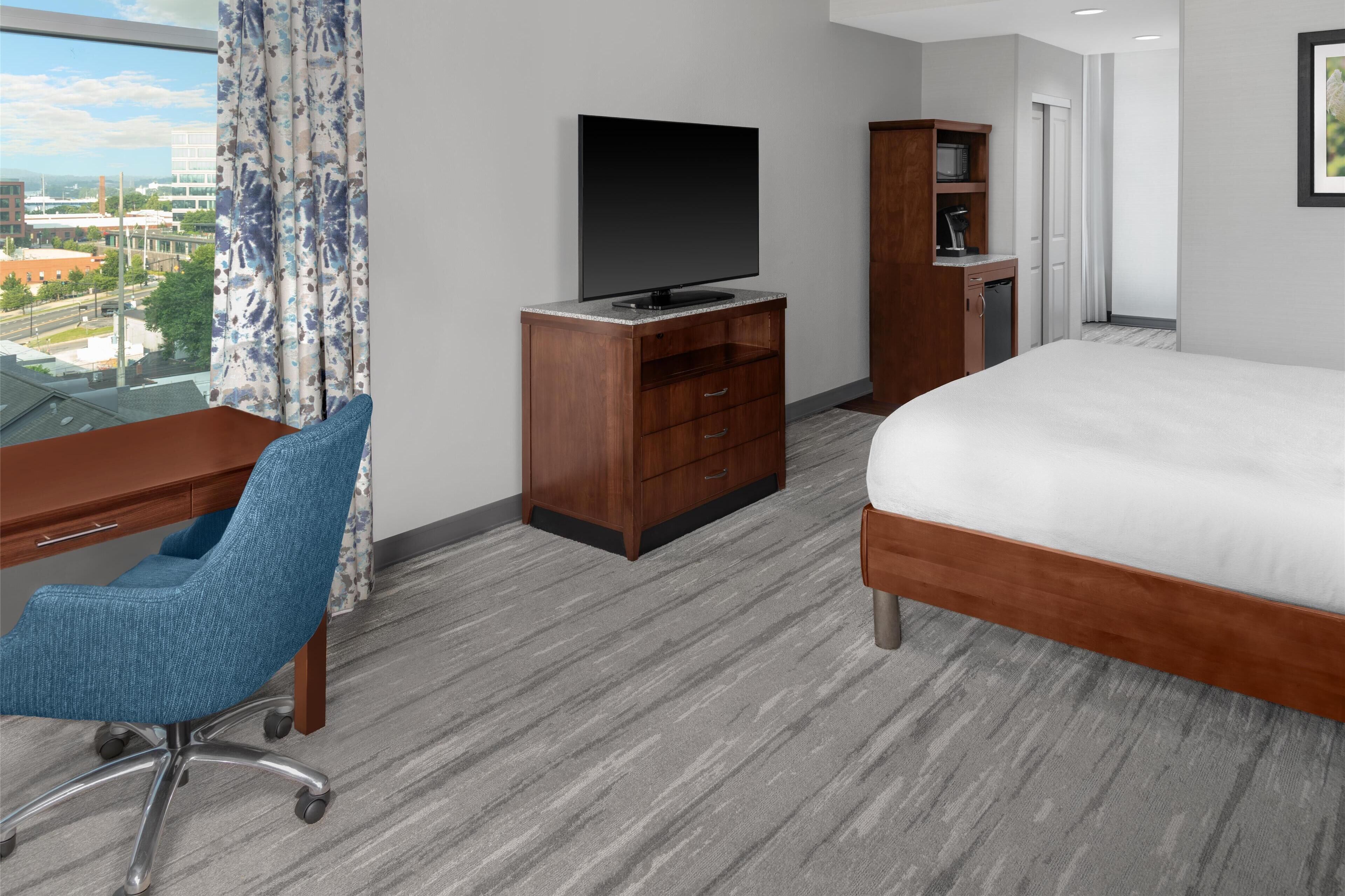 A hotel room with a large bed, a desk with a chair, a television, and a wardrobe.