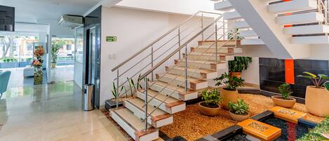 A modern lobby with a staircase, potted plants, and a water feature.
