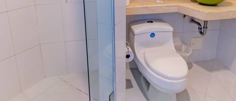 A bathroom with a glass shower enclosure, a toilet, a sink with a green basin, and a mirror above the sink.