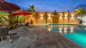 A pool area with a stone wall, outdoor seating, and a red umbrella.