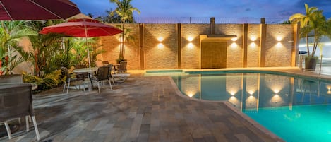 Un área de piscina con muro de piedra, mobiliario exterior y un paraguas rojo.