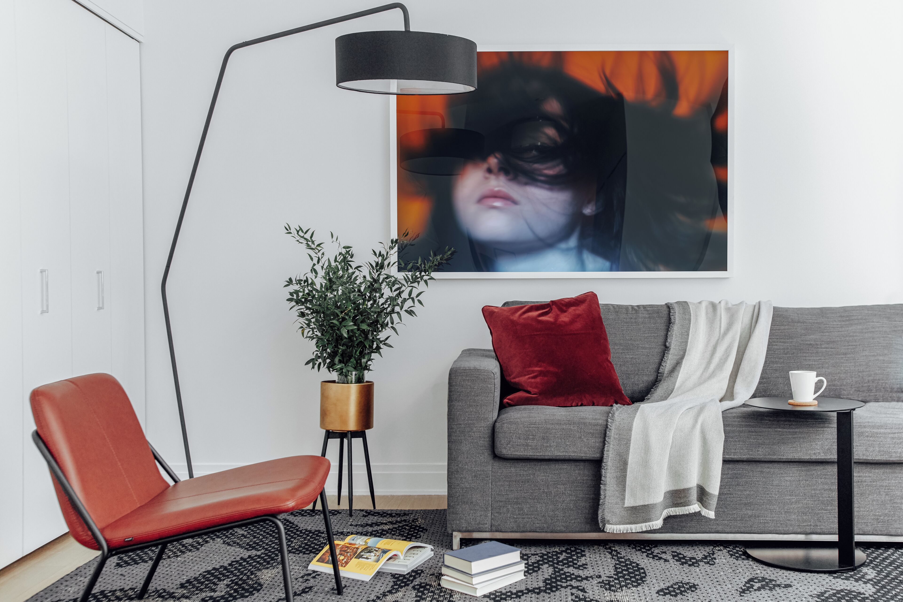 A modern living room with a sofa, a red chair, a floor lamp, a coffee table, and a large abstract painting.
