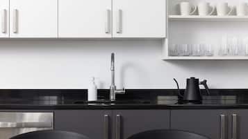 Una cocina moderna con armarios blancos, encimera negra y un lavamanos. Hay dos sillas en la mesa y un frutero con naranjas.