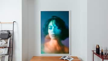 A framed portrait on a wall, a wooden side table with a book, and a metal rack with magazines.