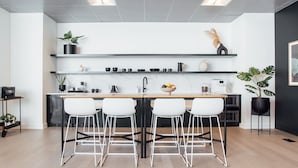 Una cocina moderna con una isla central, taburetes blancos y estanterías de metal negro.