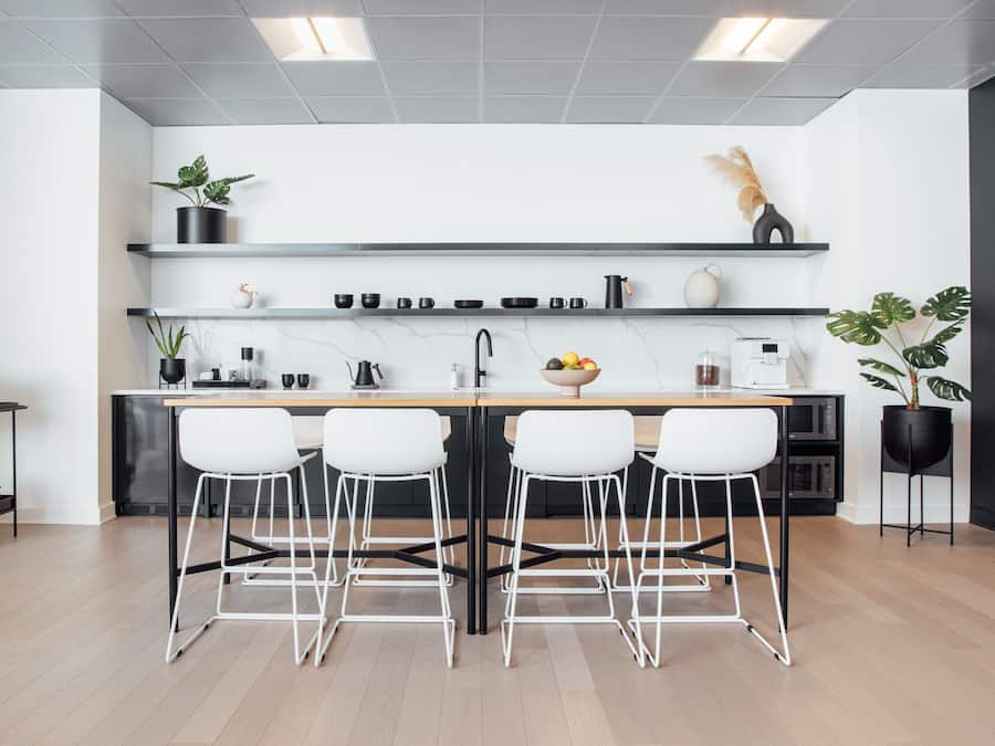 Une cuisine moderne avec un îlot central, des tabourets de bar blancs et des étagères en métal noir.