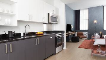 A modern kitchen with a black countertop, stainless steel appliances, and white cabinetry. There is a dining area with a table and chairs, and a large window with curtains.