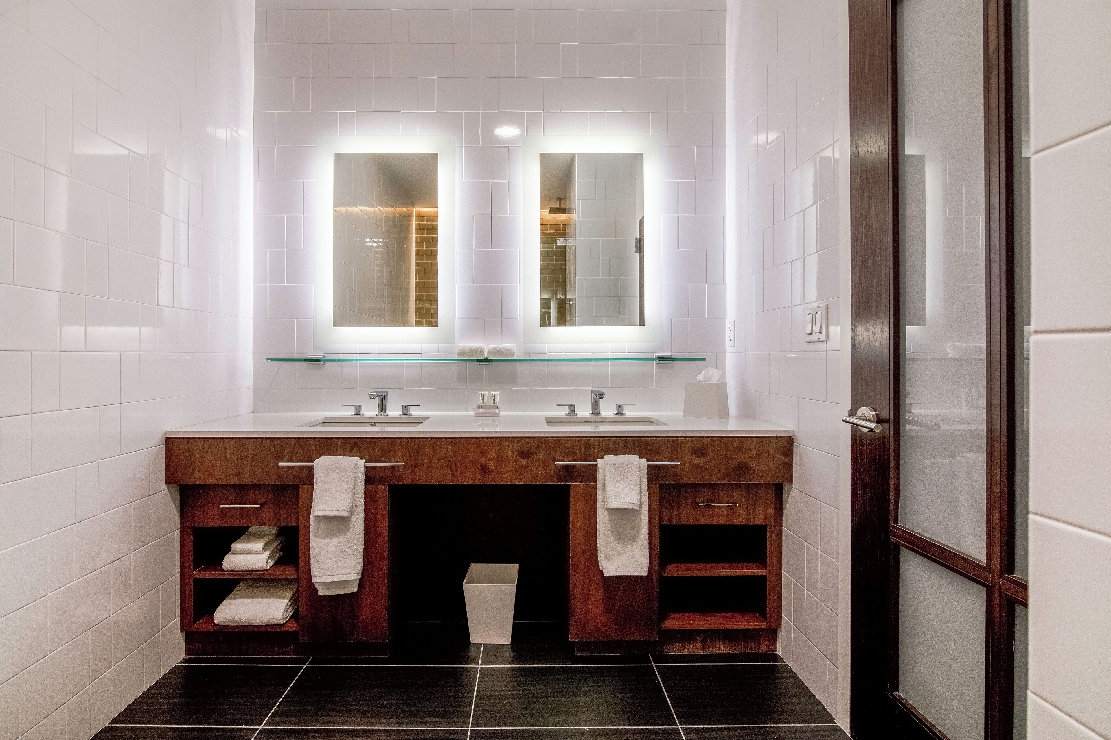 A modern bathroom with a wooden vanity, two sinks, and a glass shelf above.