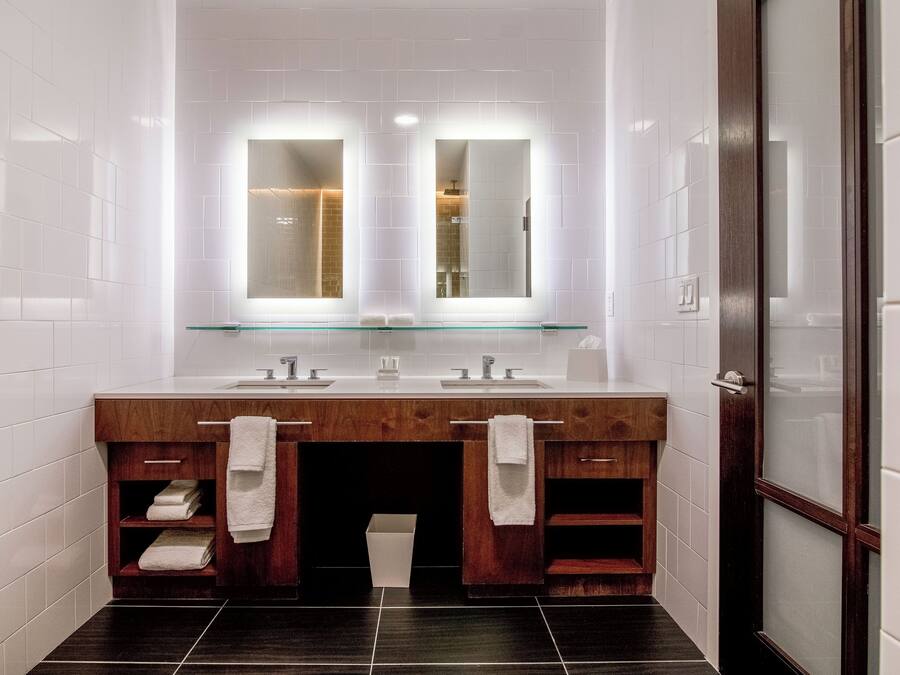A modern bathroom with a wooden vanity, two sinks, and a glass shelf above.