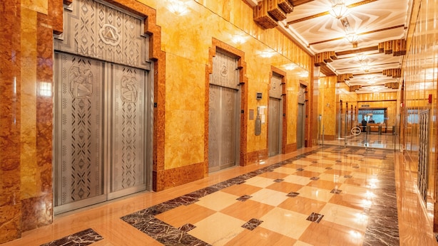 Un vestíbulo de hotel con pisos de mármol, puertas de ascensor ornamentadas y un diseño de piso a cuadros.