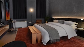 Un dormitorio moderno con una cama grande, mesitas de noche, un banco, un escritorio y una ventana con cortinas.