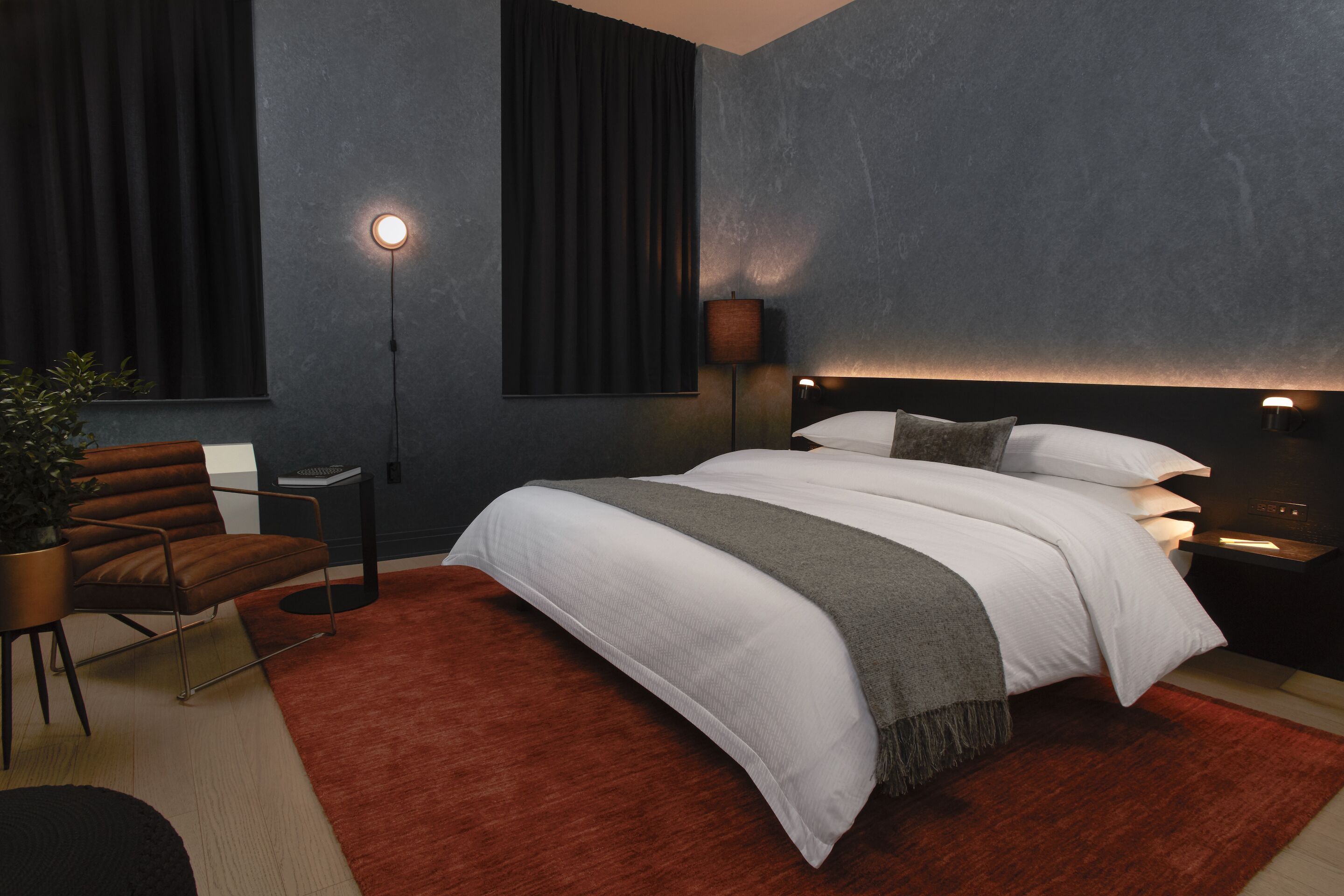 Un dormitorio moderno con una cama grande, paredes oscuras y una alfombra roja.