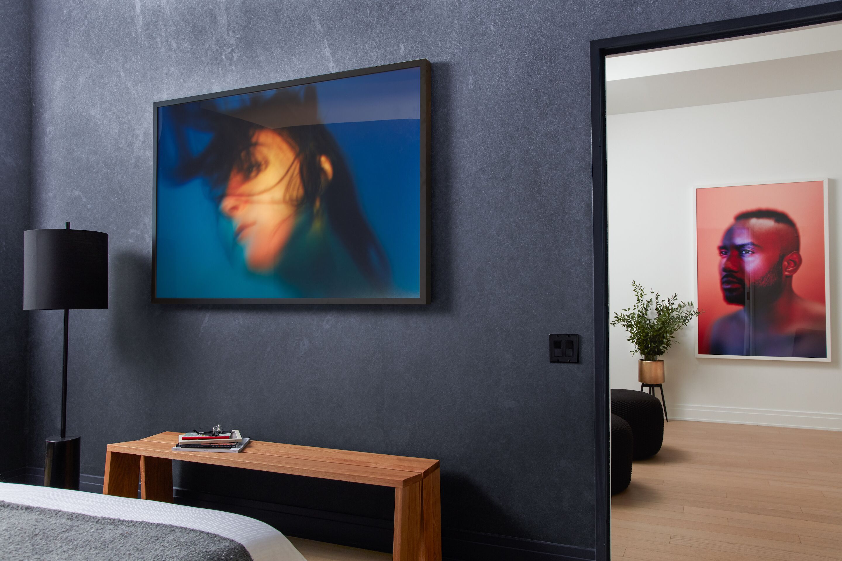 A modern bedroom with a dark textured wall, a wooden bedside table, a black floor lamp, and two framed artworks.