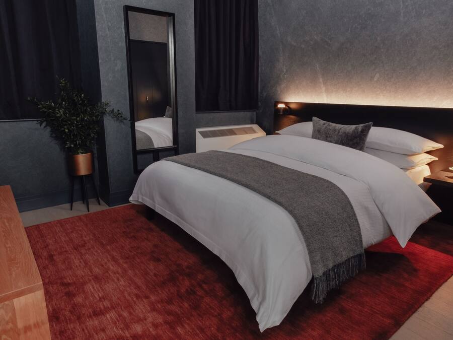 A modern bedroom with a large bed, a bedside table, a nightstand, a mirror, and a red rug.