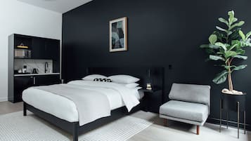 Una camera da letto moderna con una parete nera, un letto con biancheria da letto bianca, una poltrona grigia, un comodino con una lampada e una pianta.