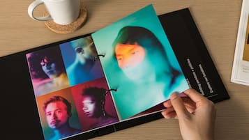 A person holding a photo album with a cork coaster and a white mug on a wooden table.