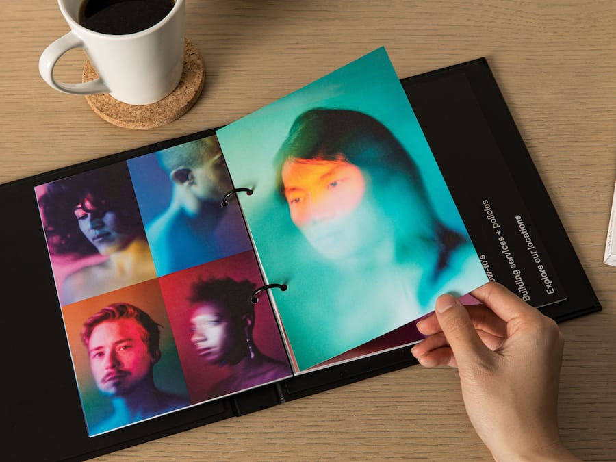 A person holding a photo album with a cork coaster and a white mug on a wooden table.