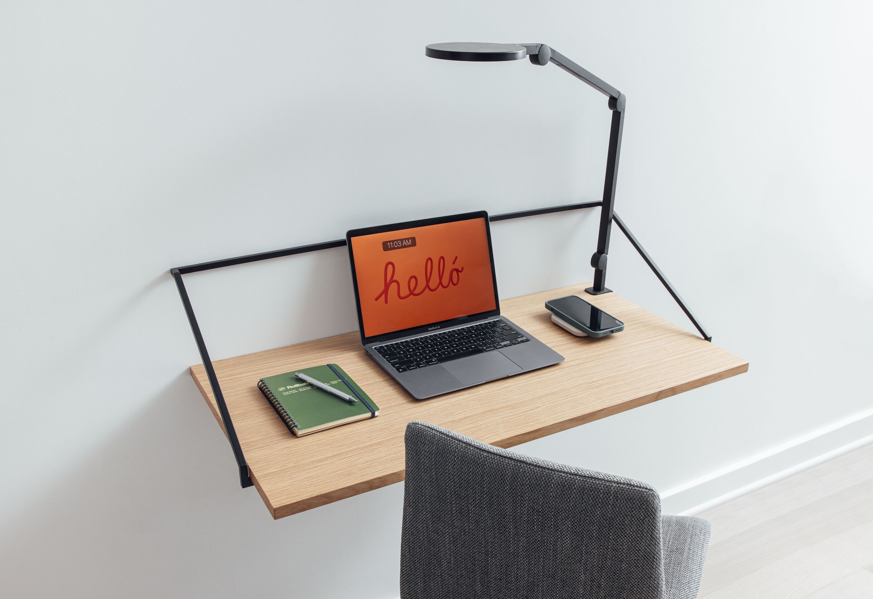 A laptop on a wooden desk with a smartphone and a notebook.