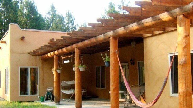 A covered outdoor area with wooden beams, potted plants, and a hammock. - Baergnaescht Bed & Breakfast (Osoyoos)