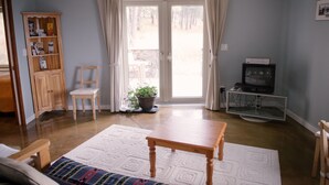 A living room with a wooden table, a sofa, a wooden cabinet, a television, and a sliding glass door leading to an outdoor area. - Baergnaescht Bed & Breakfast (Osoyoos)