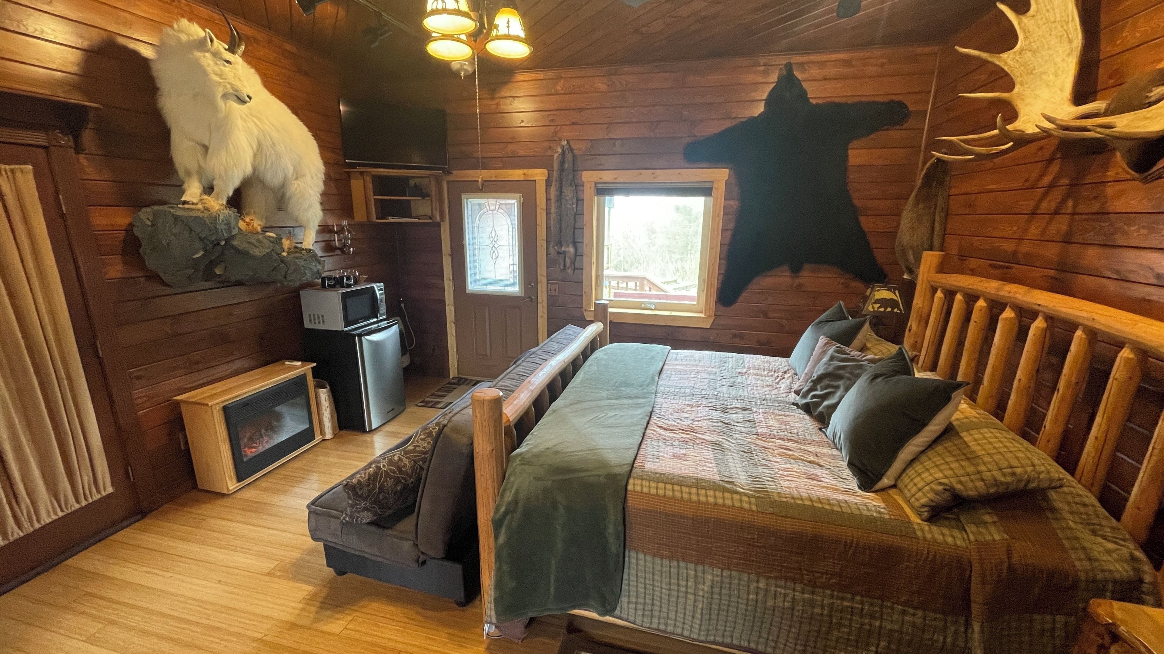 A log cabin bedroom with a bed, a small kitchenette, a mounted animal head, and a large animal head on the wall.
