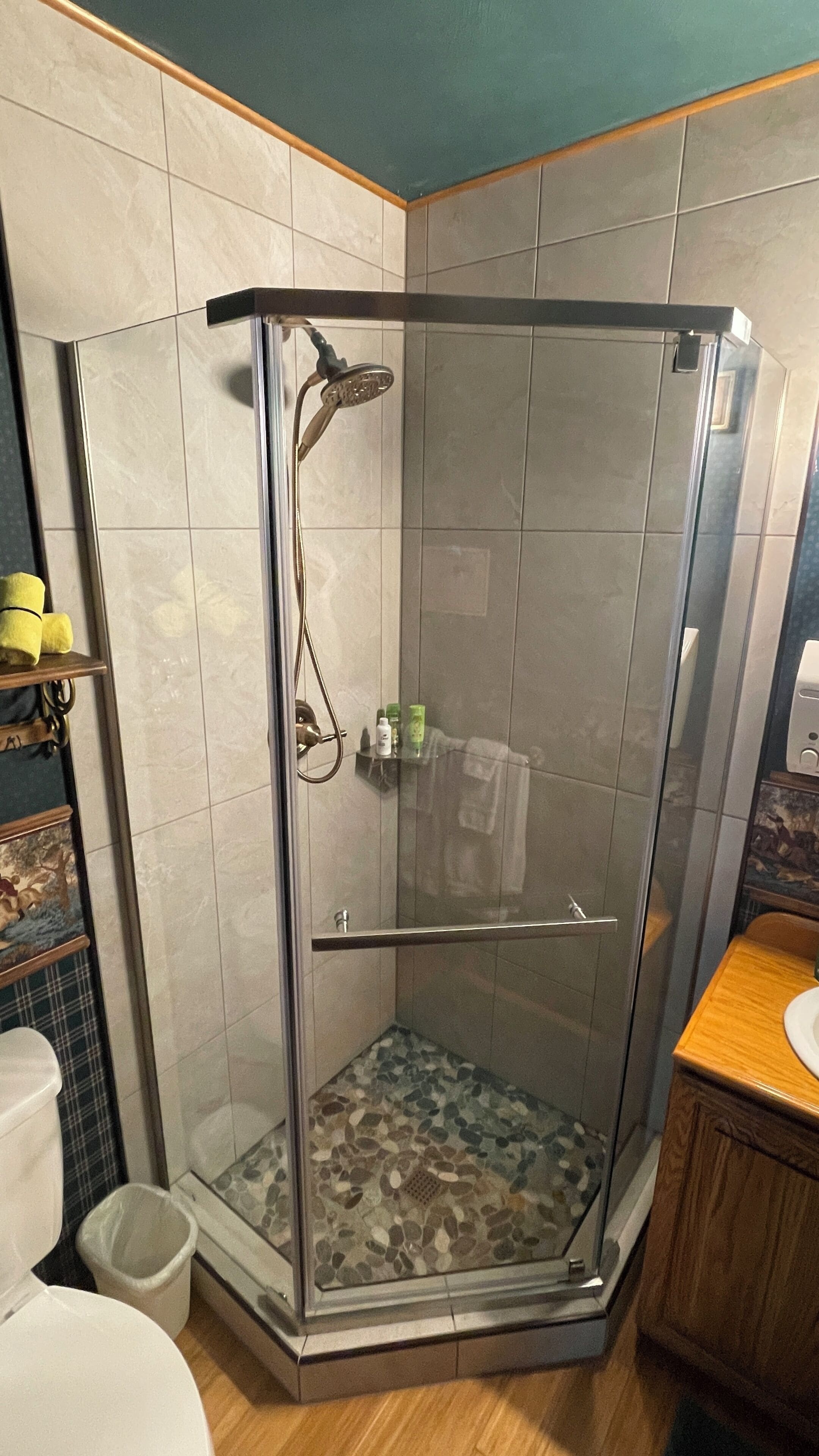 En brusekabine med glasvægge, brusehoved og en lille hylde med toiletartikler.