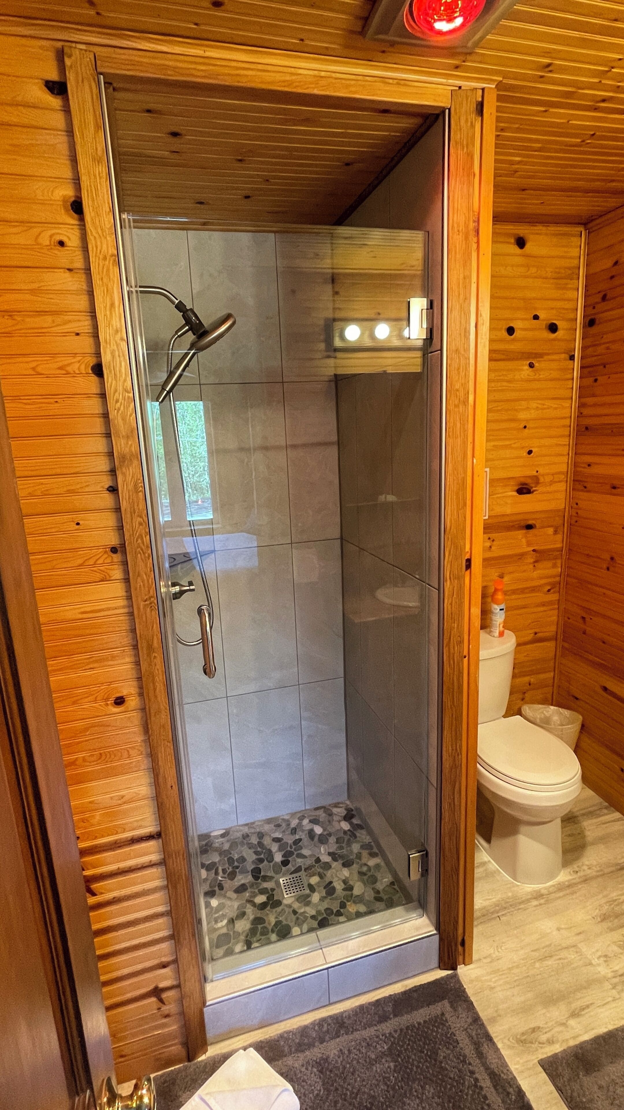 A shower with a glass door, a toilet, and a wooden interior.