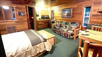 A cozy cabin-style room with a bed, a sofa, a dining table, and a kitchenette.