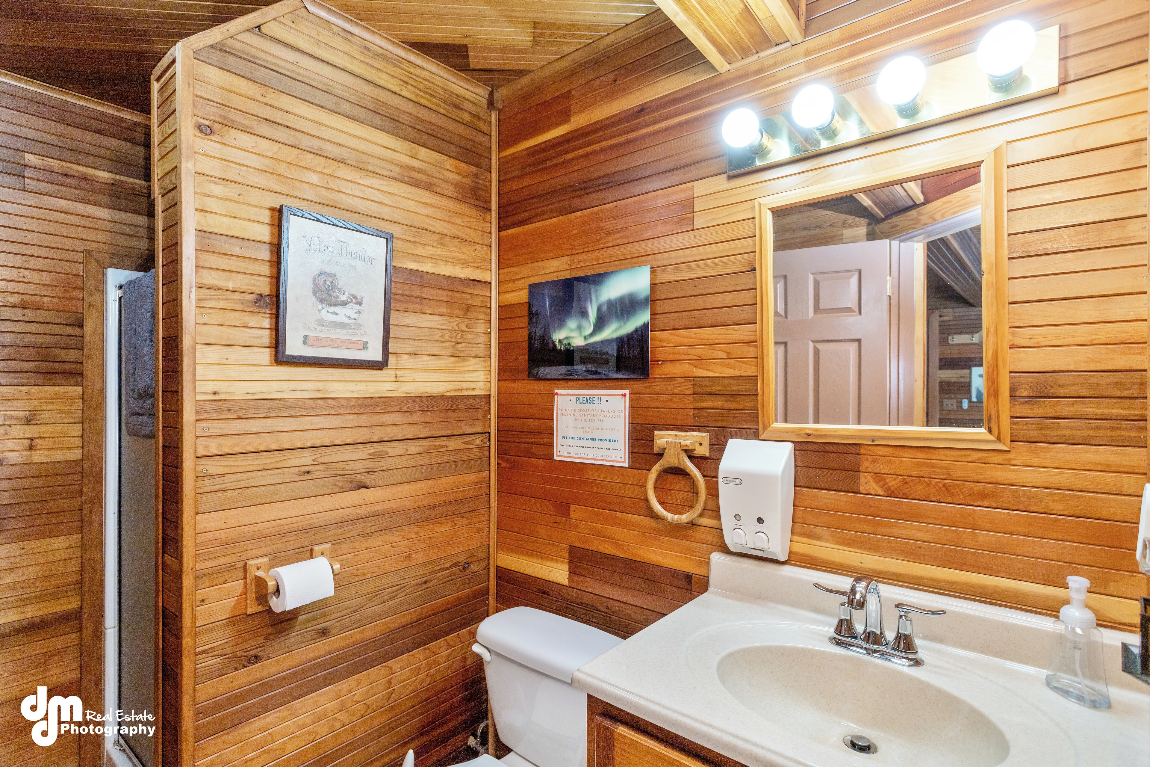 Une salle de bain rustique, aménagée dans une cabane en bois, avec des toilettes, un lavabo et un miroir.