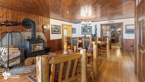 A cozy cabin interior with a wood-burning stove, wooden furniture, and a dining area. - Talkeetna Denali View Lodge and Cabins (Talkeetna)