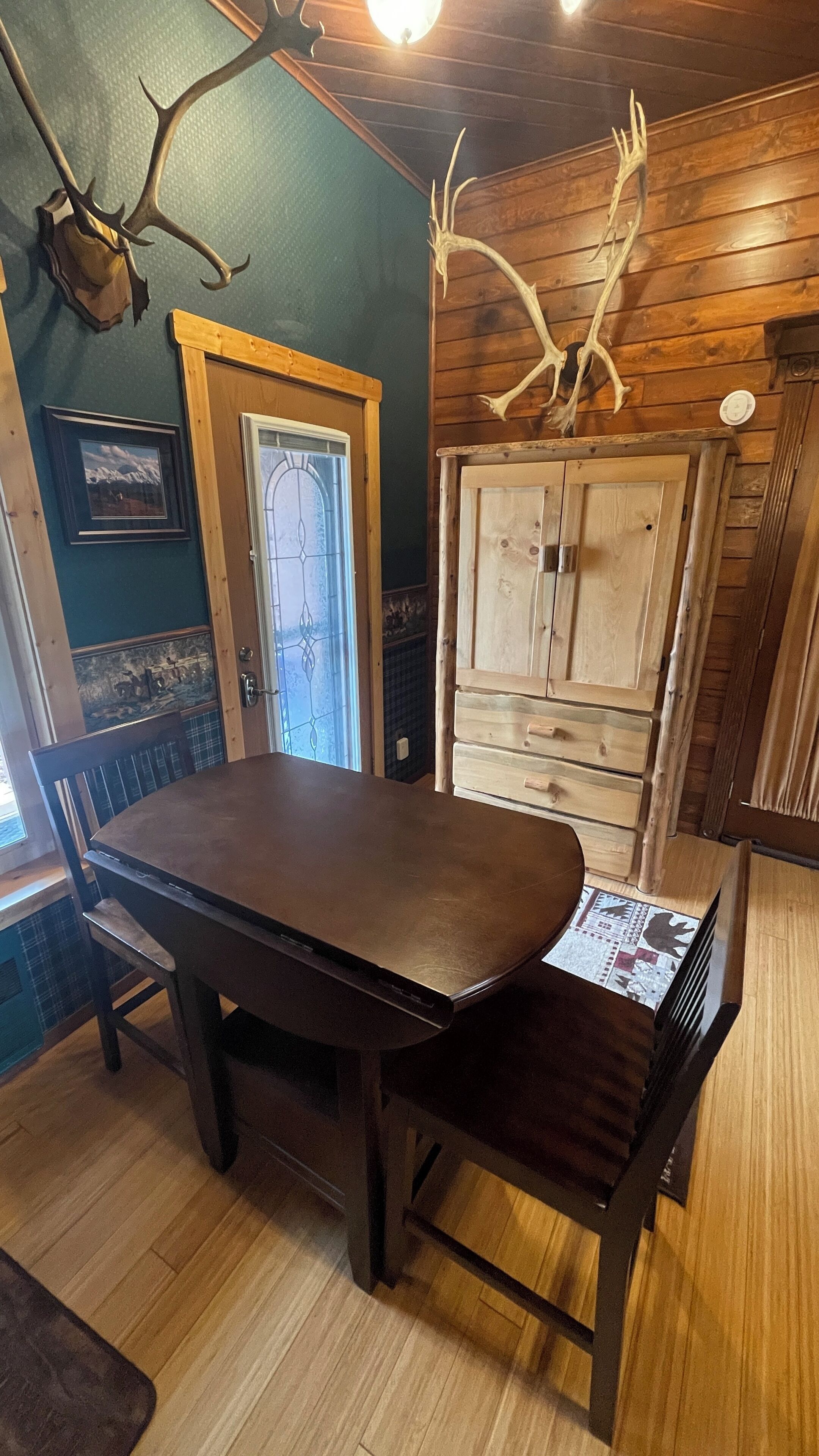 A dining area with a wooden table and chairs, a cabinet, and antlers on the wall.