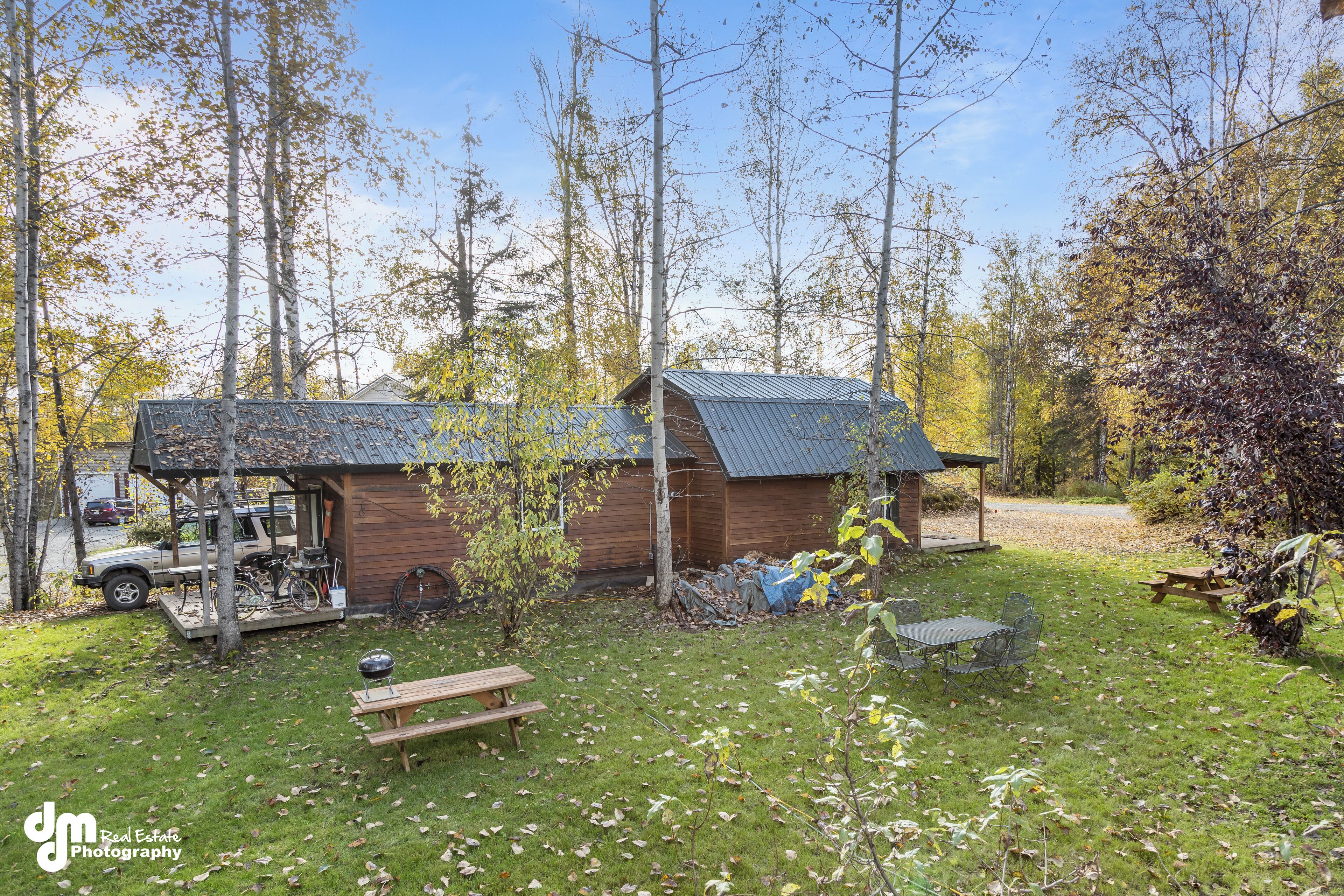 Un rustico chalet con tetto in metallo, circondato da alberi e un tavolo da picnic in un prato.