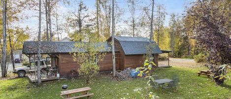 Un rustico chalet con tetto in metallo, circondato da alberi e un tavolo da picnic in un prato.