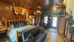 A log cabin bedroom with a large bed, a bench, and elk antlers on the walls. - Talkeetna Denali View Lodge and Cabins (Talkeetna)