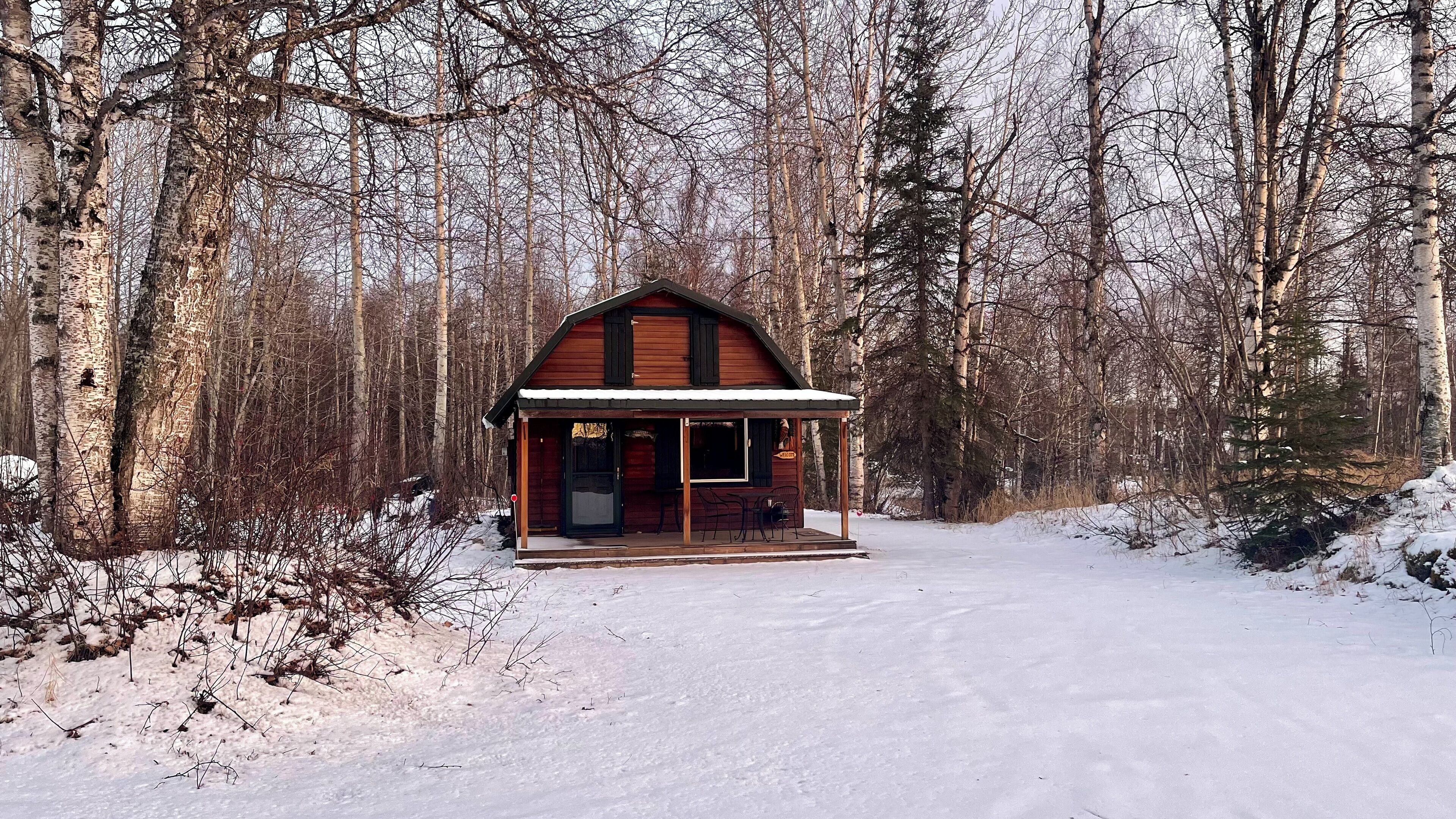 Una cabaña de madera con un porche, rodeada por un bosque nevado.