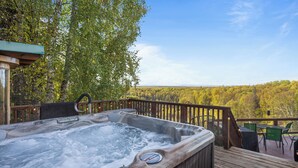 A hot tub on a wooden deck with a view of a forest. - Talkeetna Denali View Lodge and Cabins (Talkeetna)