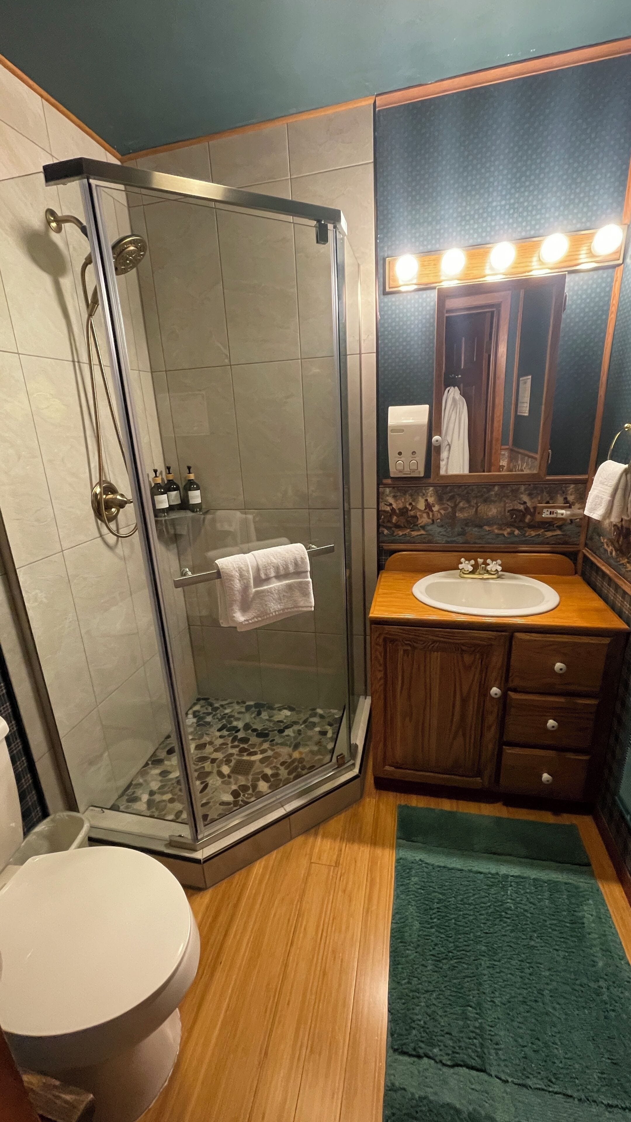 A bathroom with a glass-enclosed shower, a wooden vanity with a sink, and a mirror with lights above it.