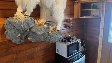 A rustic cabin interior with a large white animal head mounted on a rock, a fireplace, a television, and a refrigerator.