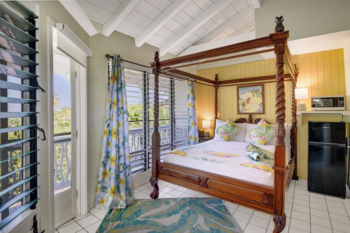 A four-poster bed with a wooden frame, a small bedside table with a lamp, and a black refrigerator.