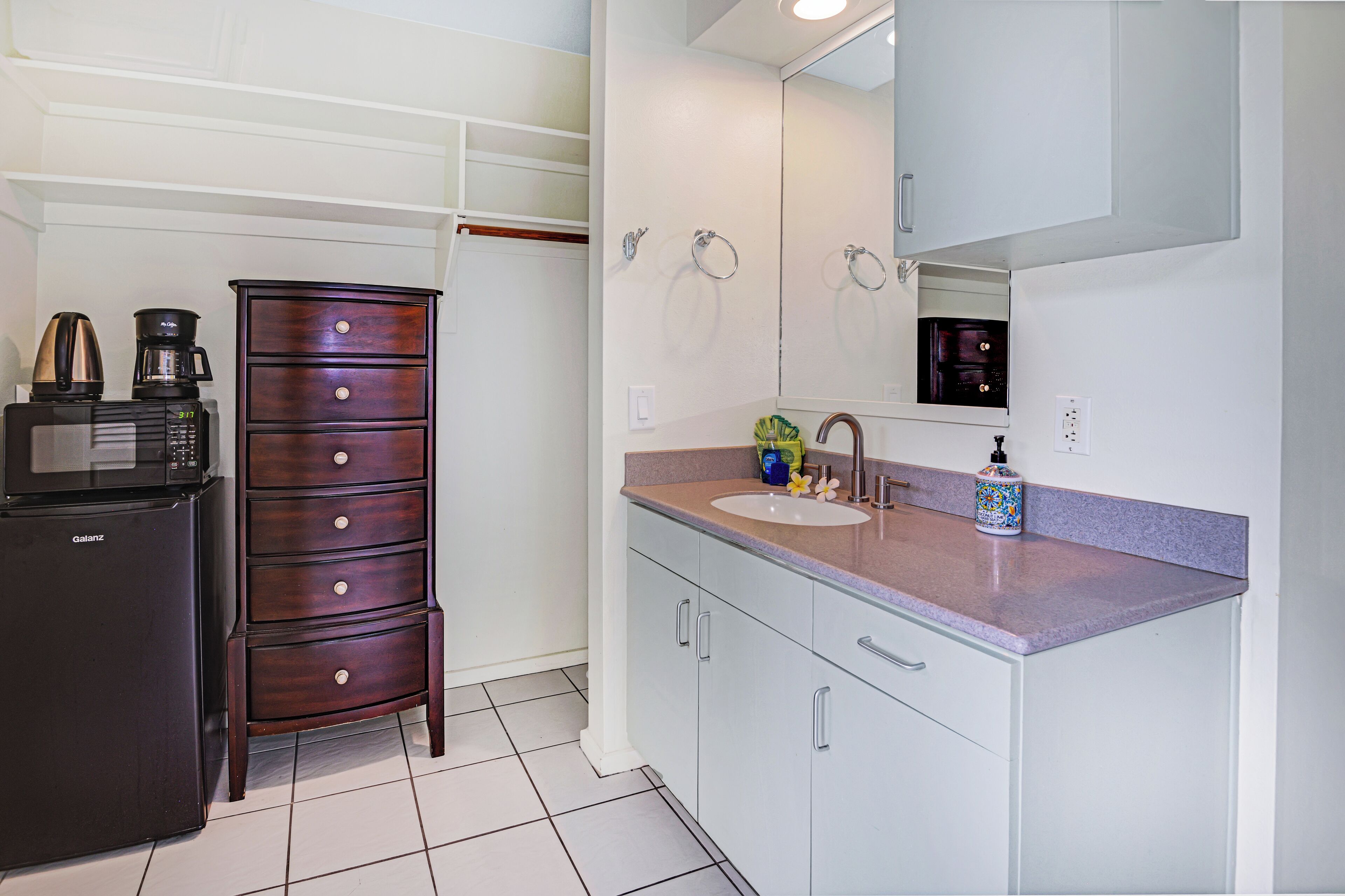 A compact kitchen with a built-in microwave, a coffee maker, and a cabinet with drawers.