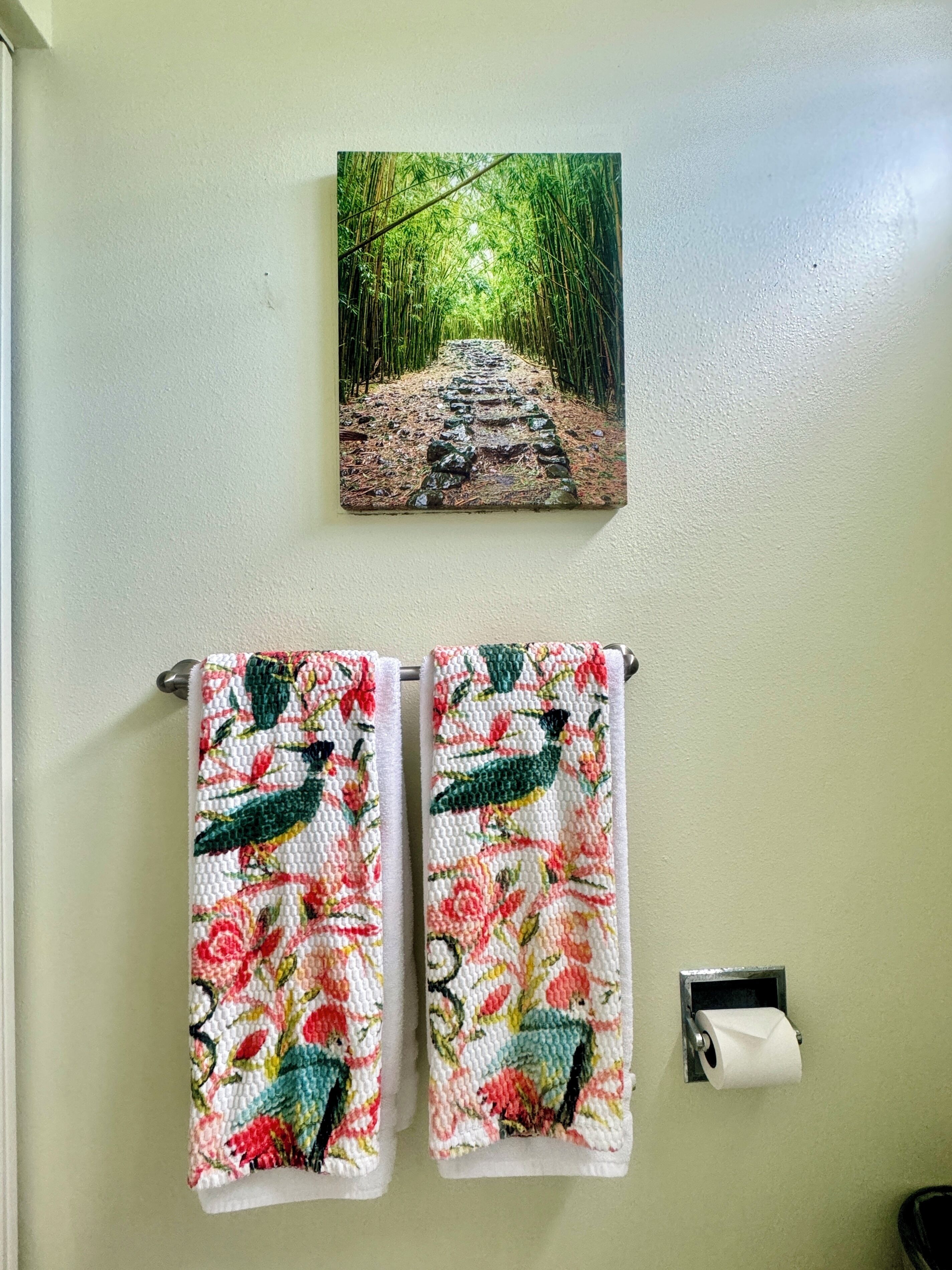 A bathroom with two towels hanging on a rack, a toilet paper holder, and a painting of a bamboo forest on the wall.