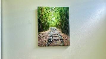 Een badkamer met twee handdoeken aan een rek, een toiletpapierhouder en een schilderij van een bamboebos op de muur.
