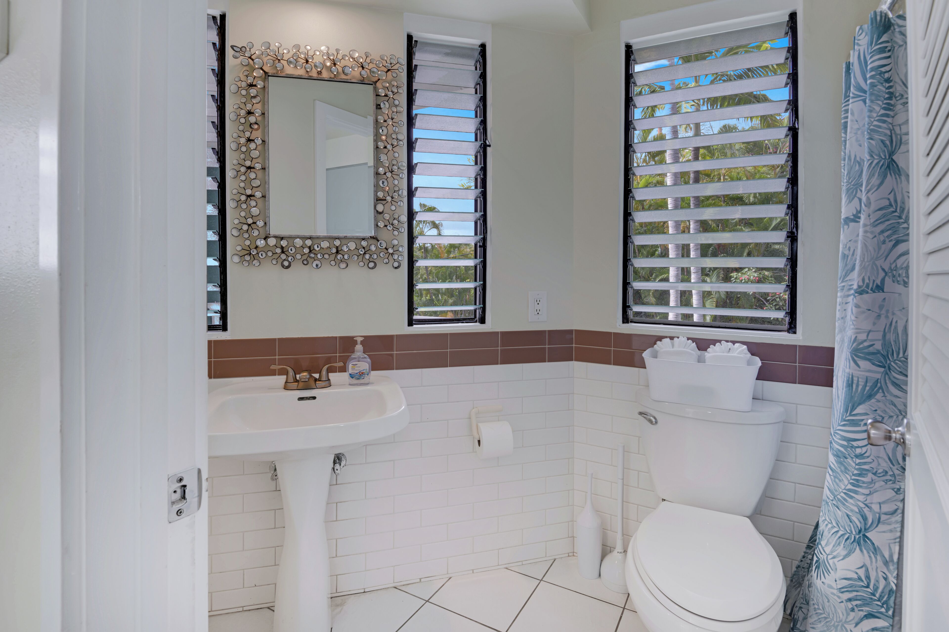 Une salle de bain avec un lavabo blanc, des toilettes et un miroir doté d’un cadre décoratif.