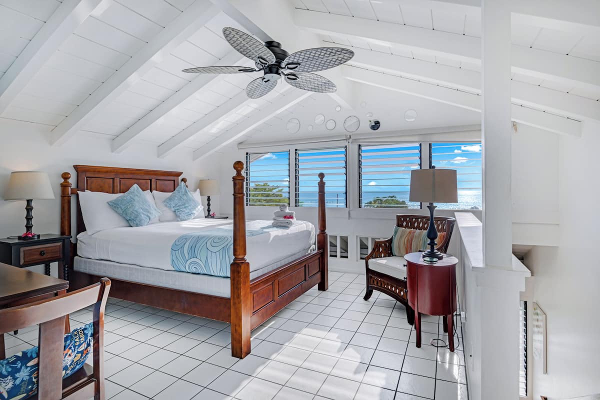 A spacious bedroom with a large bed, a ceiling fan, and a view of the ocean through the windows.