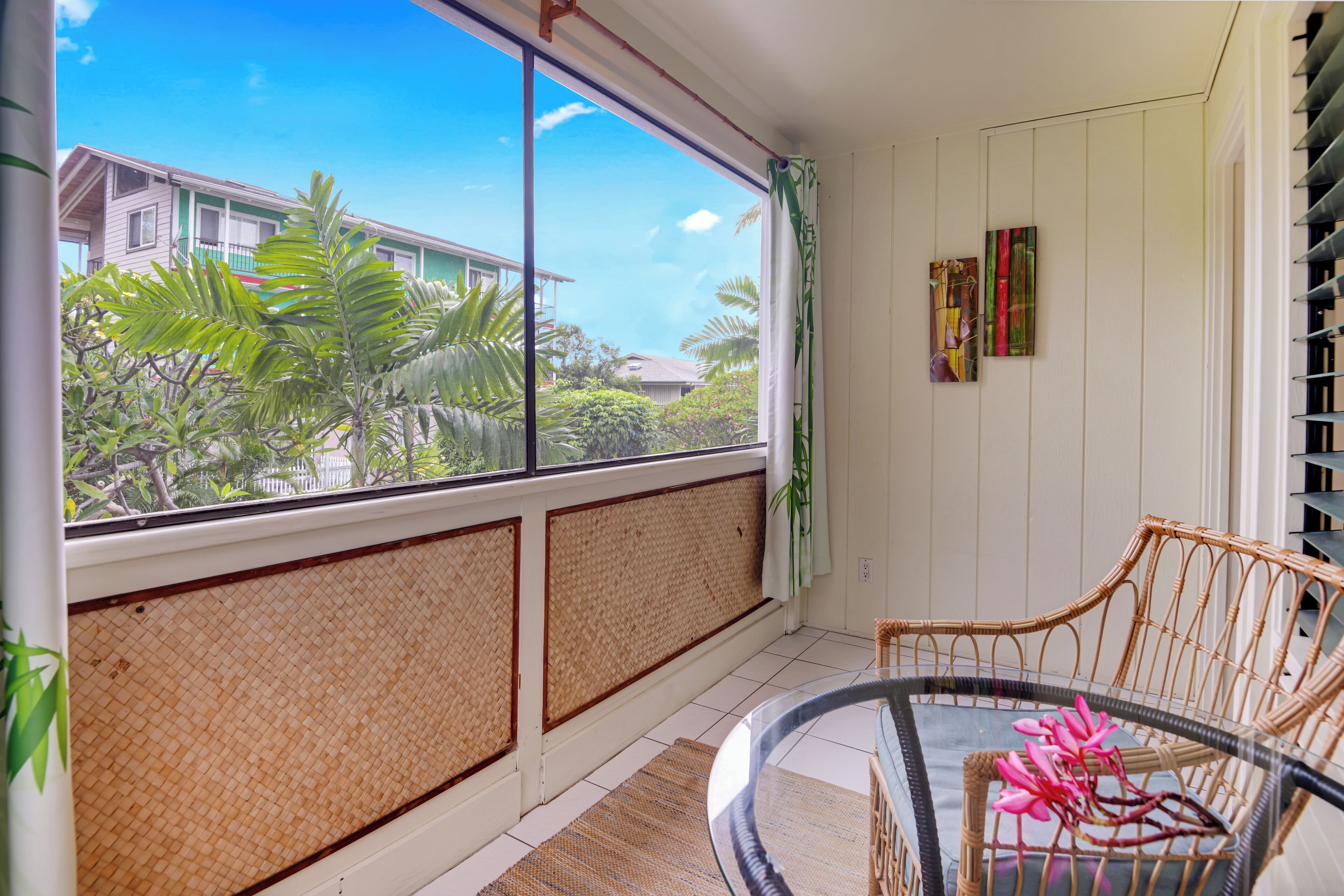 A room with a large window, wicker furniture, and a view of greenery outside.
