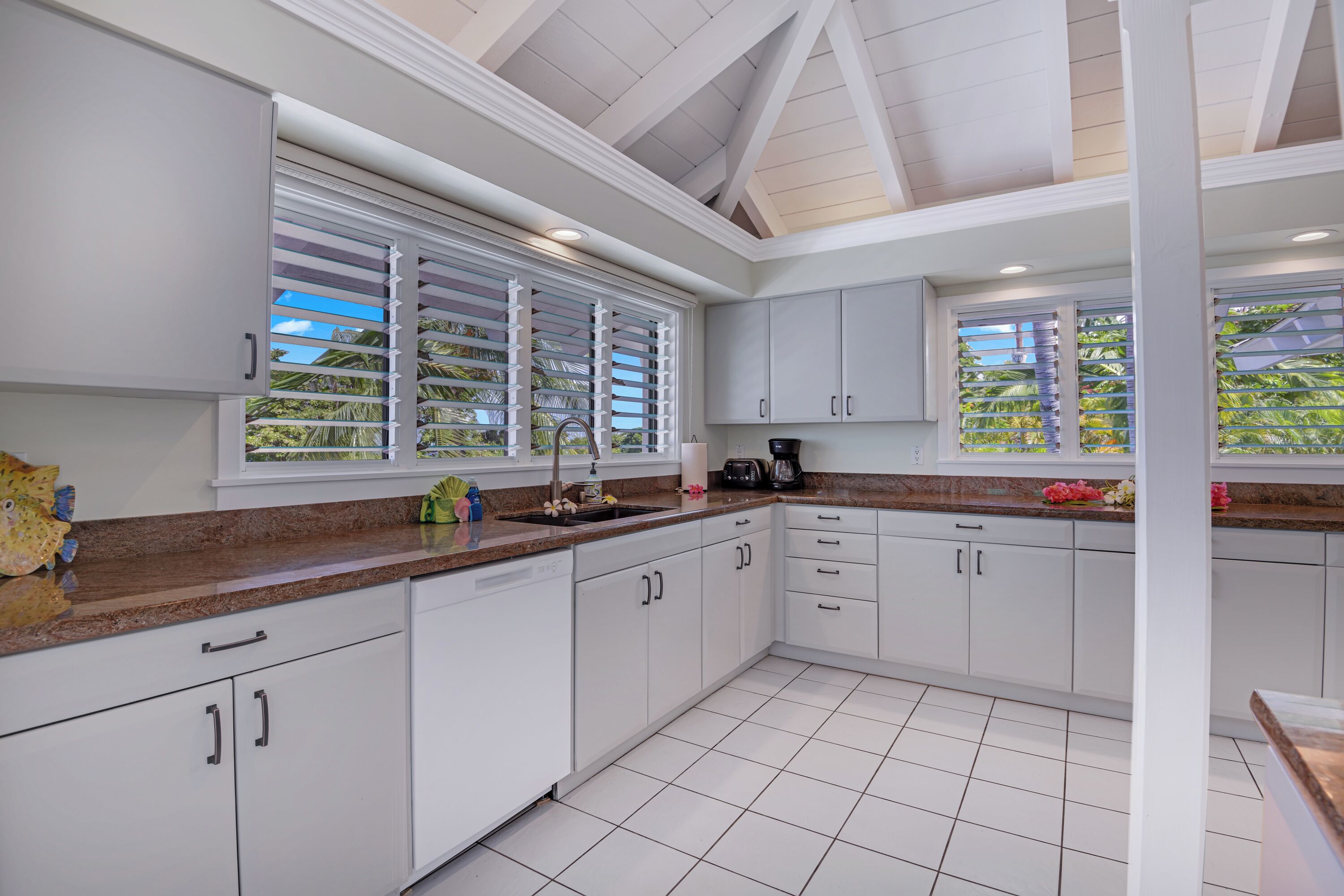 A modern kitchen with white cabinets, granite countertops, and large windows with blinds.